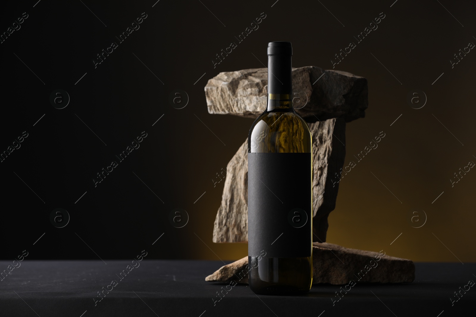 Bottle of wine and rocks on black table against dark yellow background, space for text Photo of Bottle of wine and rocks on black table against dark yellow background, space for text