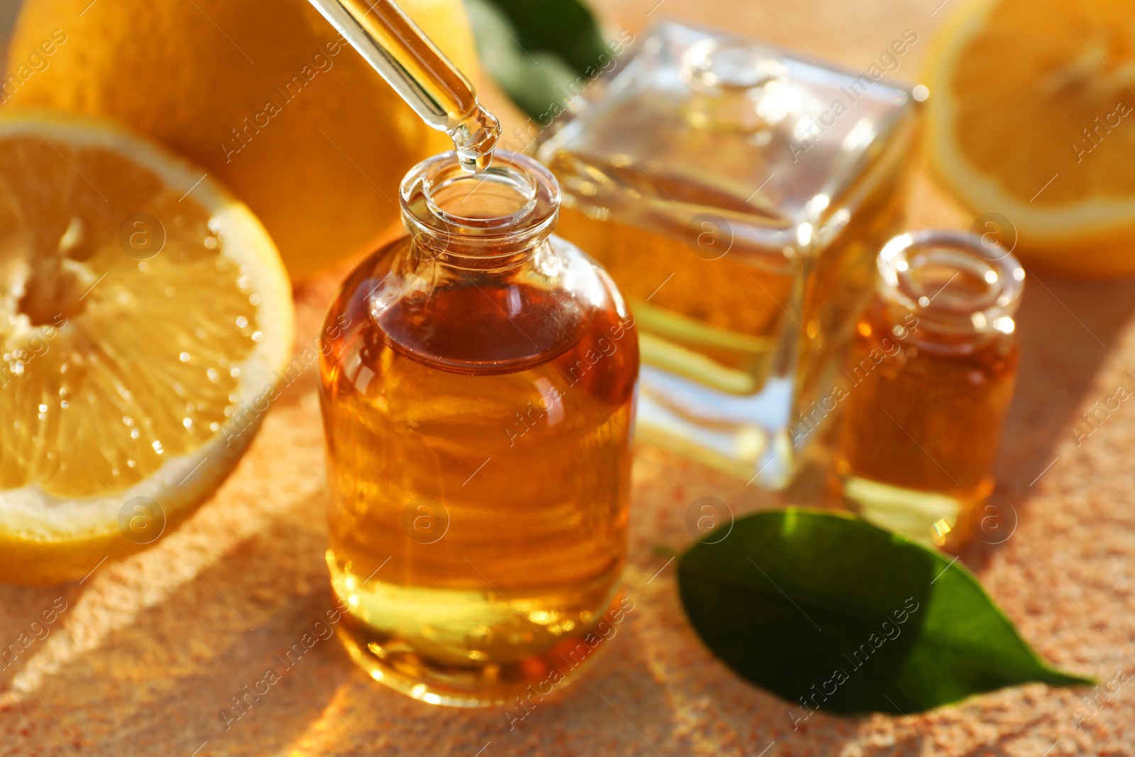 Photo of Taking aromatic oil from perfume bottle with dropper on beige textured background, closeup