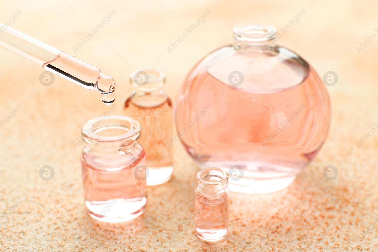 Photo of Taking aromatic oil from perfume bottle with dropper on beige textured background, closeup