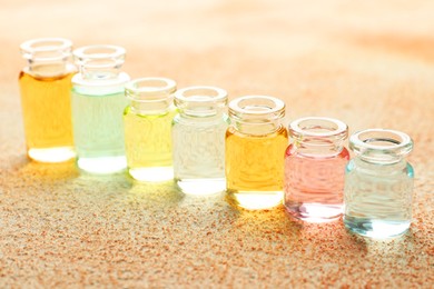 Photo of Perfume bottles with aromatic oils on beige textured background, closeup