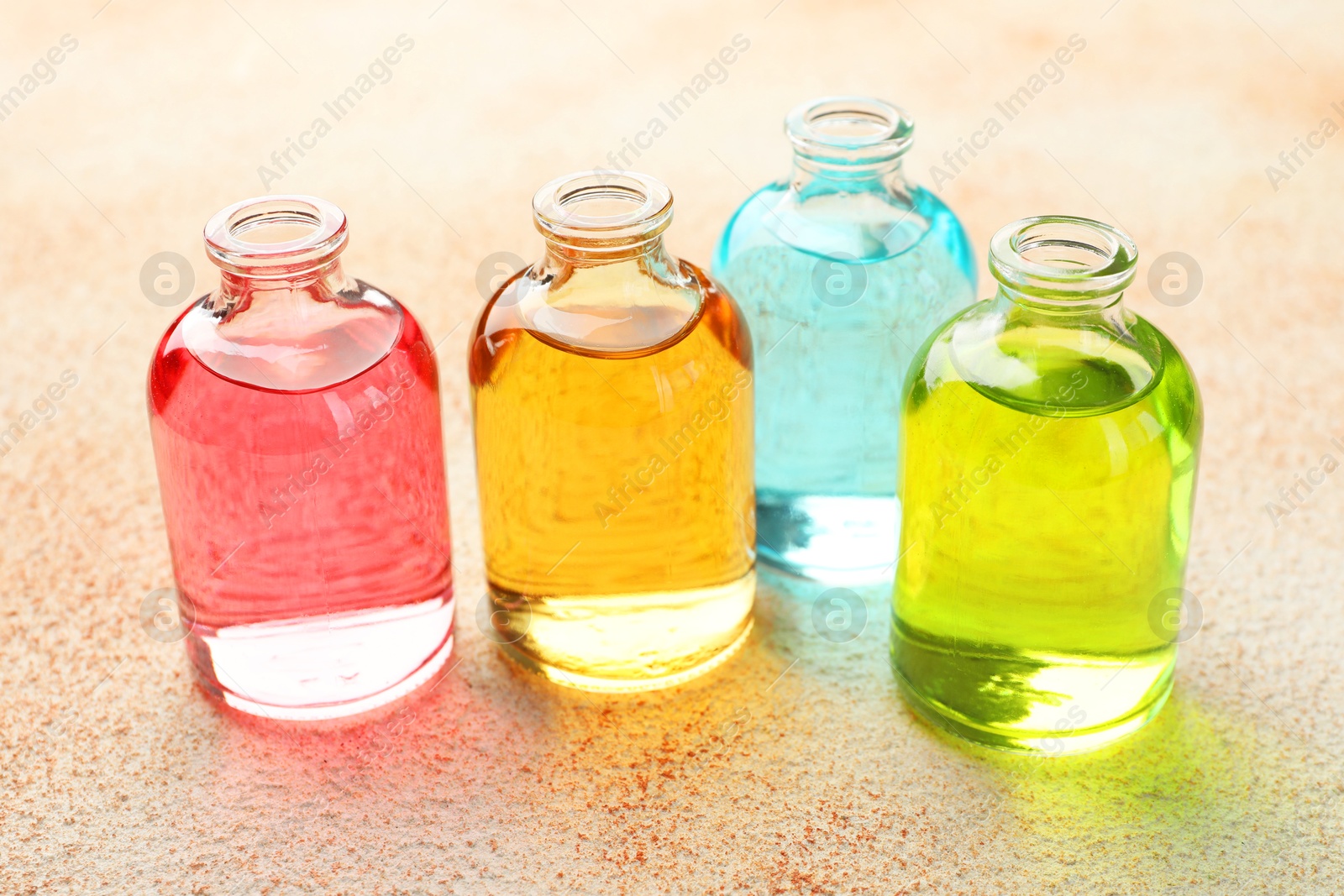 Photo of Perfume bottles with aromatic oils on beige textured background, closeup