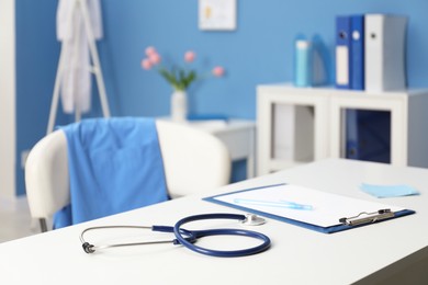 Photo of Doctor's workplace. Clipboard, other stationery and stethoscope on white table in medical office, closeup
