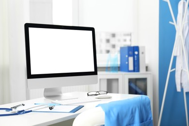 Photo of Doctor's workplace. Computer monitor, clipboard, stethoscope and glasses on white table in medical office