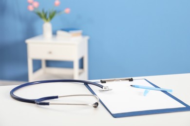 Photo of Doctor's workplace. Stethoscope, clipboard and pen on white table in medical office, closeup. Space for text
