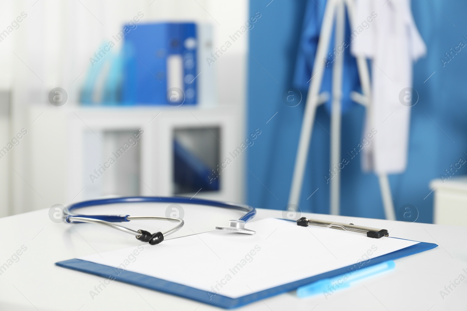Photo of Doctor's workplace. Stethoscope, clipboard and pen on white table in medical office, closeup. Space for text