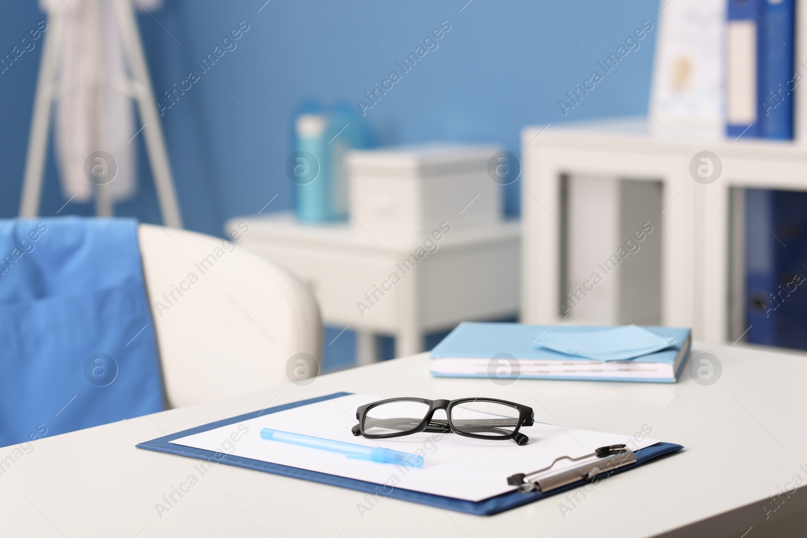 Doctor's workplace. Clipboard, other stationery and glasses on white table in medical office Photo of Doctor's workplace. Clipboard, other stationery and glasses on white table in medical office