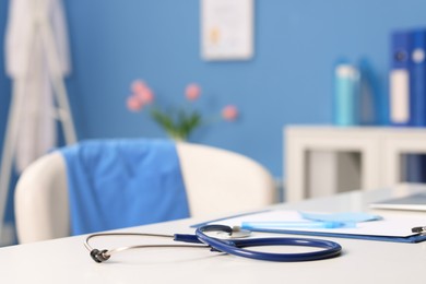 Photo of Doctor's workplace. Stethoscope, clipboard and pen on white table in medical office, closeup