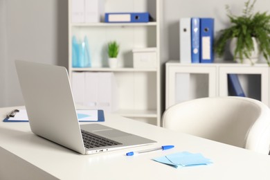 Photo of Doctor's workplace. Laptop, pen and sticky notes on white table in medical office