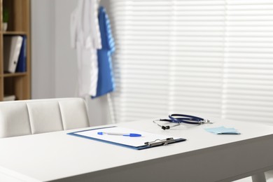 Photo of Doctor's workplace. Stethoscope, clipboard and other stationery on white table in medical office