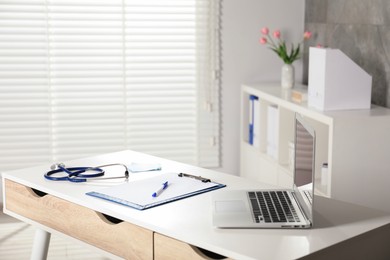 Photo of Doctor's workplace. Laptop, stationery and stethoscope on white table in medical office