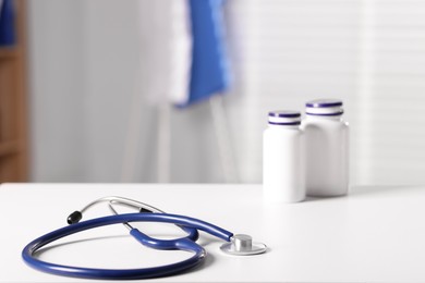 Photo of Doctor's workplace. Stethoscope and bottles of pills on white table in medical office, closeup