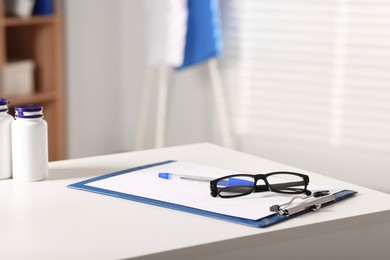 Photo of Doctor's workplace. Clipboard, pen and glasses on white table in medical office, closeup