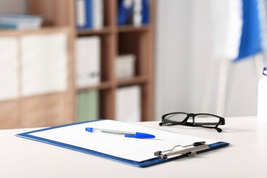 Photo of Doctor's workplace. Clipboard, pen and glasses on white table in medical office, closeup