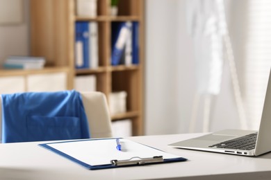 Photo of Doctor's workplace. Clipboard, pen and laptop on white table in medical office, closeup