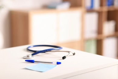 Photo of Doctor's workplace. Stethoscope, pen and sticky note on white table in medical office, closeup. Space for text