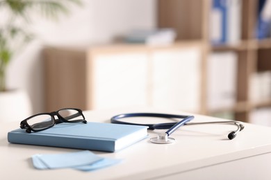 Photo of Doctor's workplace. Stethoscope, glasses and stationery on white table in medical office, closeup. Space for text