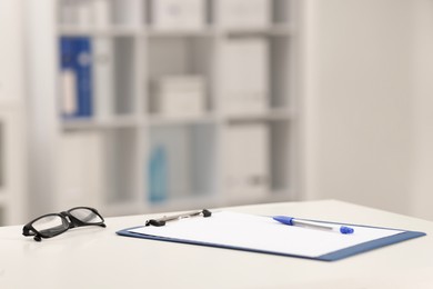 Photo of Doctor's workplace. Clipboard, pen and glasses on white table in medical office, space for text