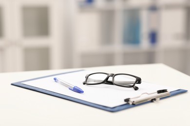 Photo of Doctor's workplace. Clipboard, pen and glasses on white table in medical office, closeup. Space for text