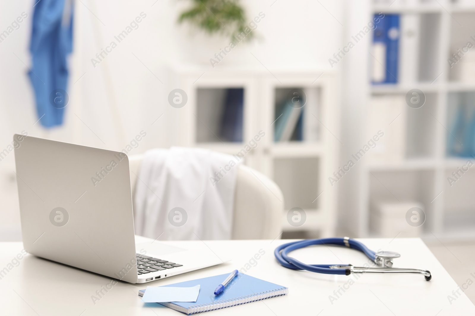 Doctor's workplace. Laptop, stethoscope and stationery on white table in medical office Photo of Doctor's workplace. Laptop, stethoscope and stationery on white table in medical office