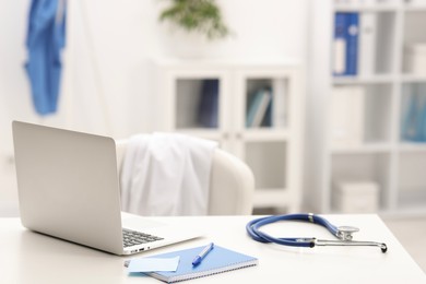 Photo of Doctor's workplace. Laptop, stethoscope and stationery on white table in medical office