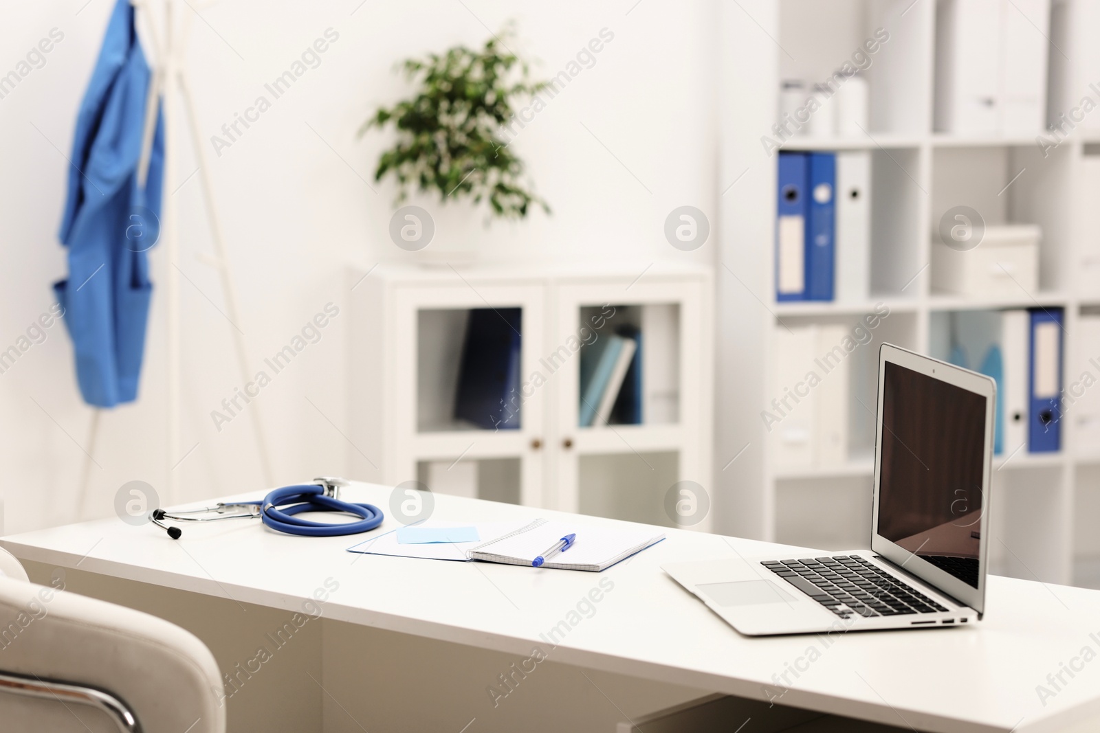 Doctor's workplace. Laptop, stethoscope and stationery on white table in medical office Photo of Doctor's workplace. Laptop, stethoscope and stationery on white table in medical office