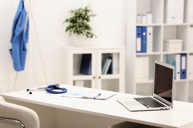 Photo of Doctor's workplace. Laptop, stethoscope and stationery on white table in medical office