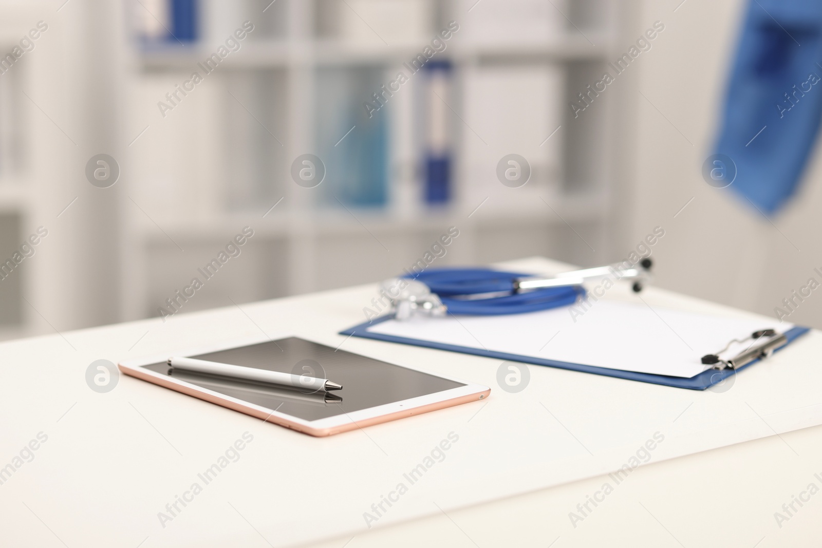 Doctor's workplace. Tablet, clipboard, pen and stethoscope on white table in medical office, closeup. Space for text Photo of Doctor's workplace. Tablet, clipboard, pen and stethoscope on white table in medical office, closeup. Space for text