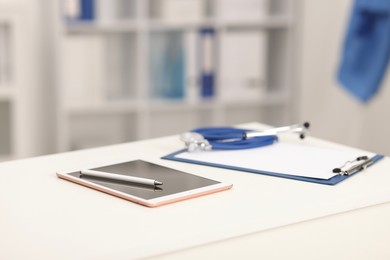 Photo of Doctor's workplace. Tablet, clipboard, pen and stethoscope on white table in medical office, closeup. Space for text