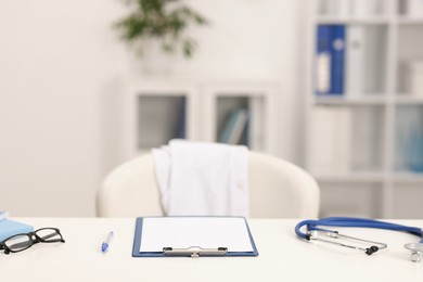 Photo of Doctor's workplace. Clipboard, other stationery, stethoscope and glasses on white table in medical office