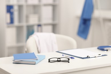 Photo of Doctor's workplace. Clipboard, other stationery and glasses on white table in medical office