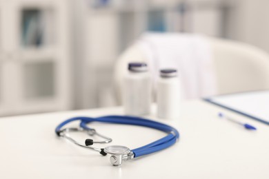 Photo of Doctor's workplace. Stethoscope and bottles of pills on white table in medical office, closeup. Space for text