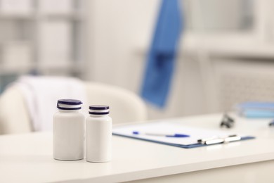 Photo of Doctor's workplace. Bottles of pills and clipboard on white table in medical office, space for text