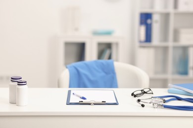 Photo of Doctor's workplace. Bottles of pills, stethoscope, glasses and clipboard on white table in medical office