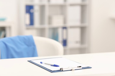 Photo of Doctor's workplace. Clipboard and pen on white table in medical office, closeup. Space for text
