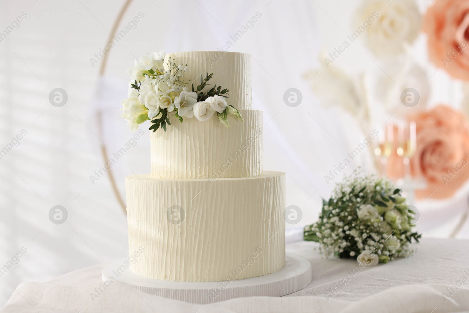 Photo of Delicious wedding cake with floral decor and bouquet on table indoors