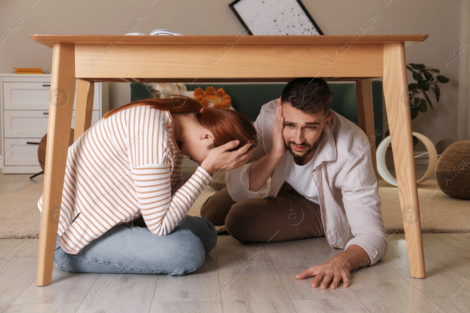 Scared couple hiding under table in living room during earthquake Photo of Scared couple hiding under table in living room during earthquake