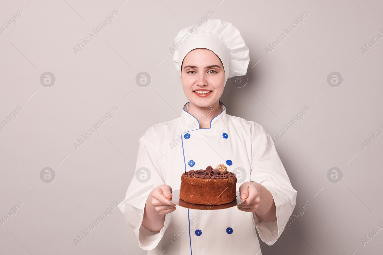 Confectioner in uniform holding delicious chocolate cake on light grey background Photo of Confectioner in uniform holding delicious chocolate cake on light grey background