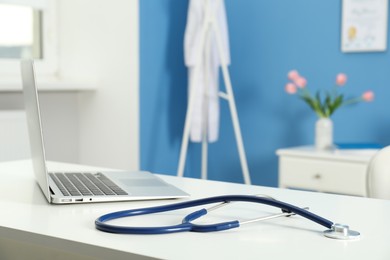 Photo of Doctor's workplace. Laptop and stethoscope on white table in medical office, closeup