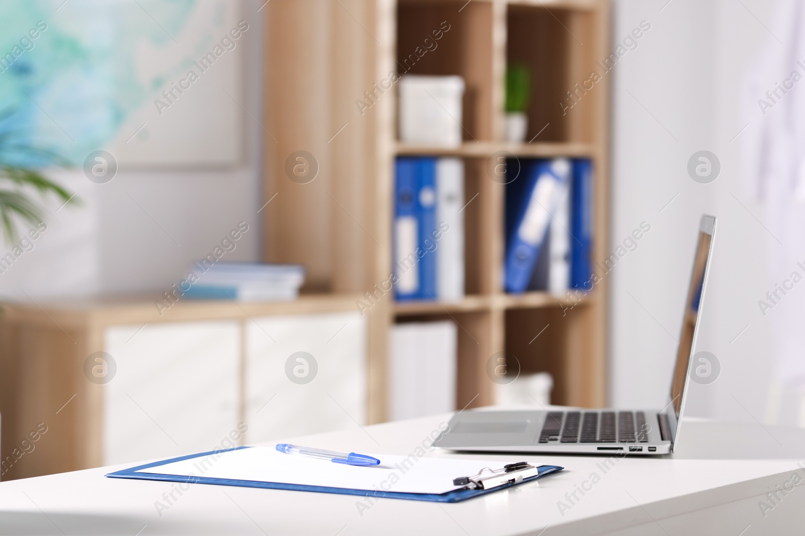 Doctor's workplace. Clipboard, pen and laptop on white table in medical office Photo of Doctor's workplace. Clipboard, pen and laptop on white table in medical office