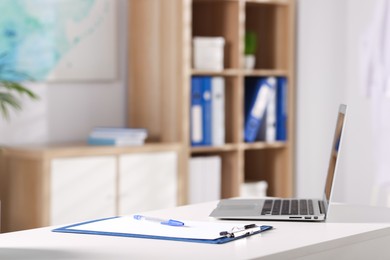 Photo of Doctor's workplace. Clipboard, pen and laptop on white table in medical office