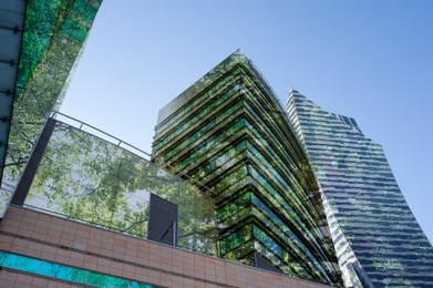 Image of Modern buildings and lush trees against blue sky, double exposure. Low angle view