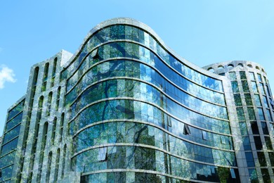 Image of Modern building and green tree against blue sky, double exposure. Low angle view