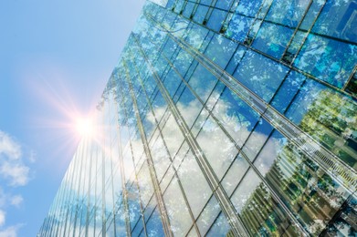 Image of Modern skyscraper and lush trees against blue sky, double exposure. Low angle view