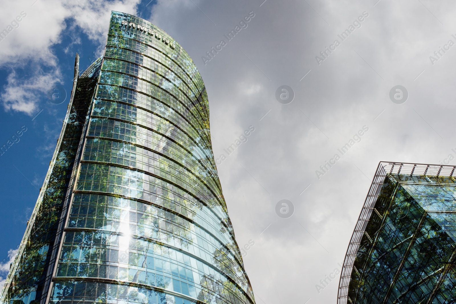 Modern buildings and green trees against cloudy sky, double exposure. Low angle view Image of Modern buildings and green trees against cloudy sky, double exposure. Low angle view