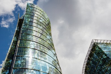 Image of Modern buildings and green trees against cloudy sky, double exposure. Low angle view