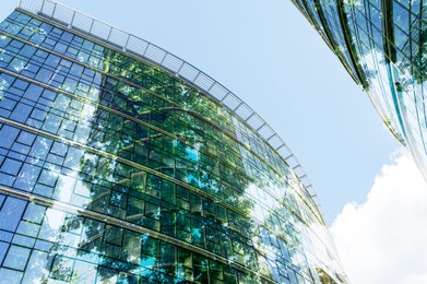 Image of Modern buildings and green trees against blue sky, double exposure. Low angle view