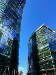 Image of Modern skyscrapers and lush trees against blue sky, double exposure. Low angle view