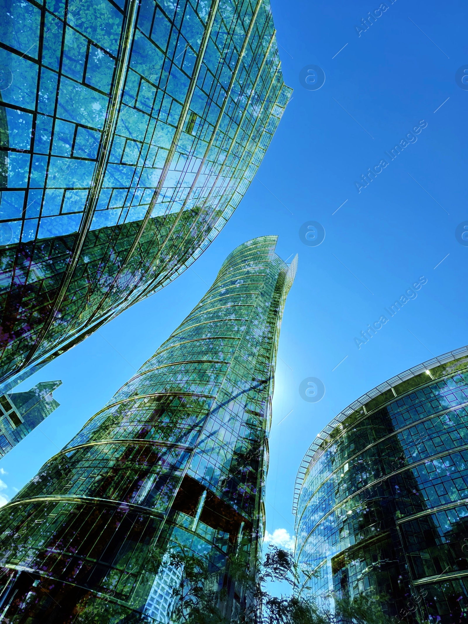Modern buildings and lush trees against blue sky, double exposure. Low angle view Image of Modern buildings and lush trees against blue sky, double exposure. Low angle view