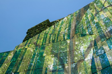 Image of Modern building and lush tree against blue sky, double exposure. Low angle view