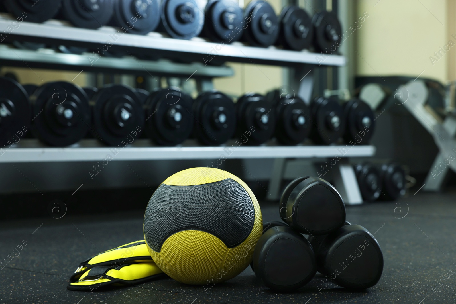 Yellow medicine ball, ankle weights and dumbbells on floor in gym Photo of Yellow medicine ball, ankle weights and dumbbells on floor in gym